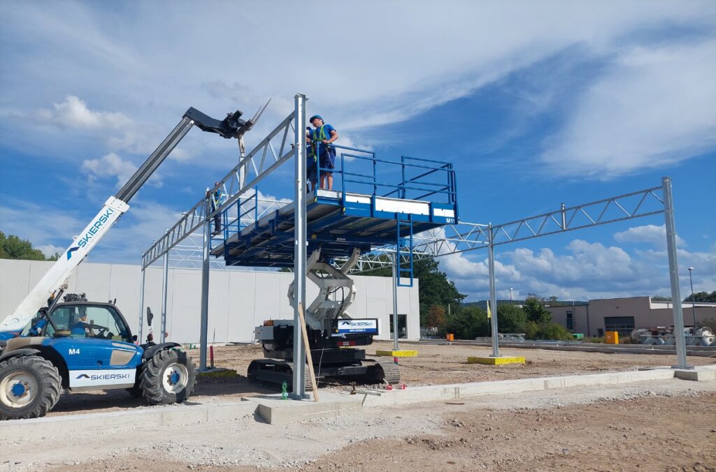 Montaż konstrukcji stalowej na placu budowy z wykorzystaniem podnośnika.