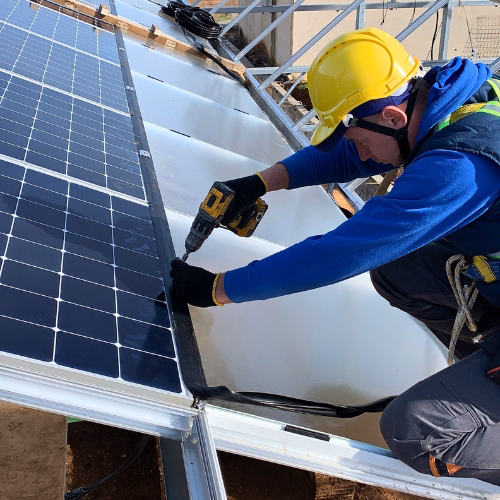 Pracownik w stroju ochronnym podczas montażu konstrukcji i paneli w szklarni.