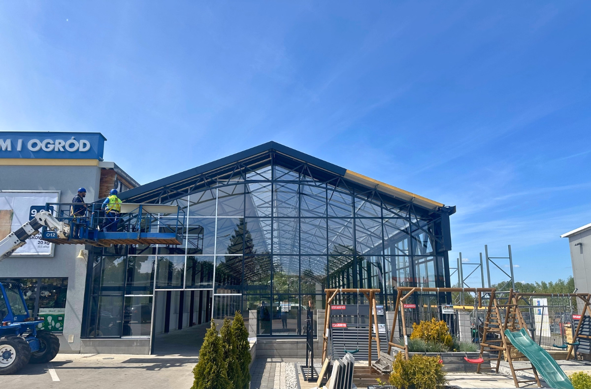 Pracownicy wykonują prace wykończeniowe na zewnątrz budynku centrum ogrodniczego.