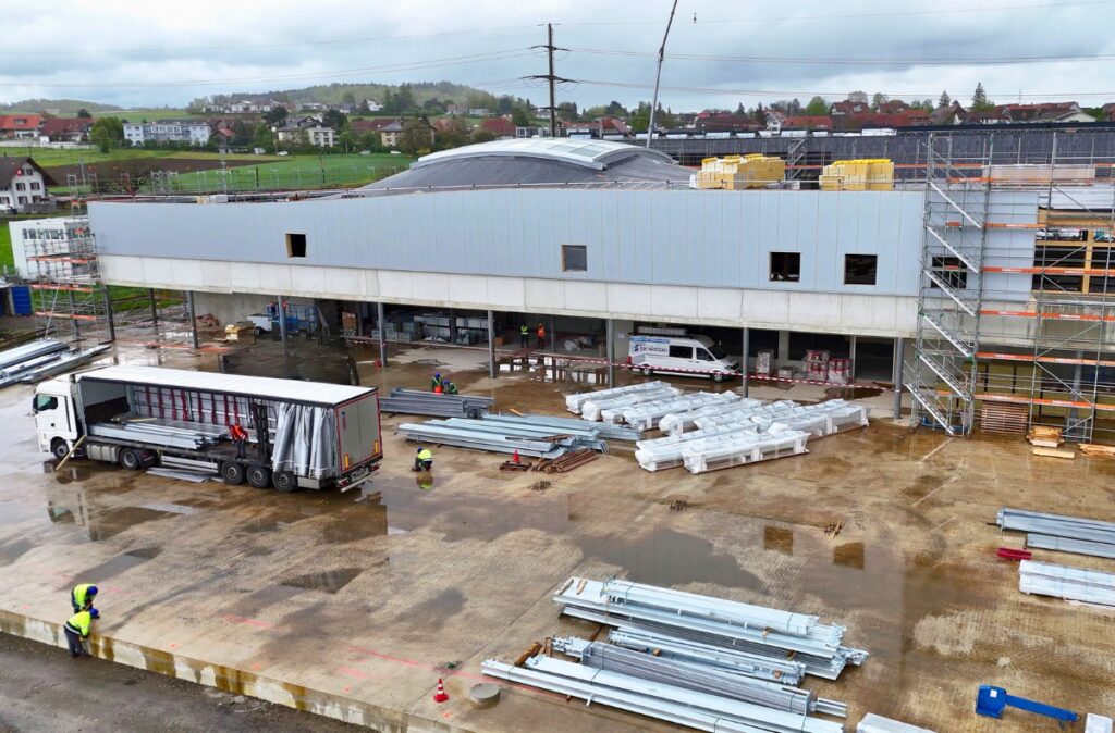 Plac budowy z przygotowaną betonową płytą i dostawą elementów konstrukcyjnych przed rozpoczęciem montażu centrum ogrodniczego.