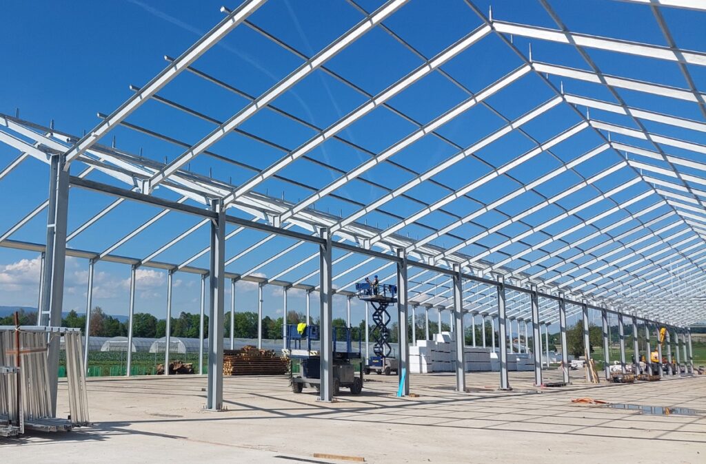 Początkowy etap montażu konstrukcji stalowej centrum ogrodniczego, ustawione słupy i wiązary główne.