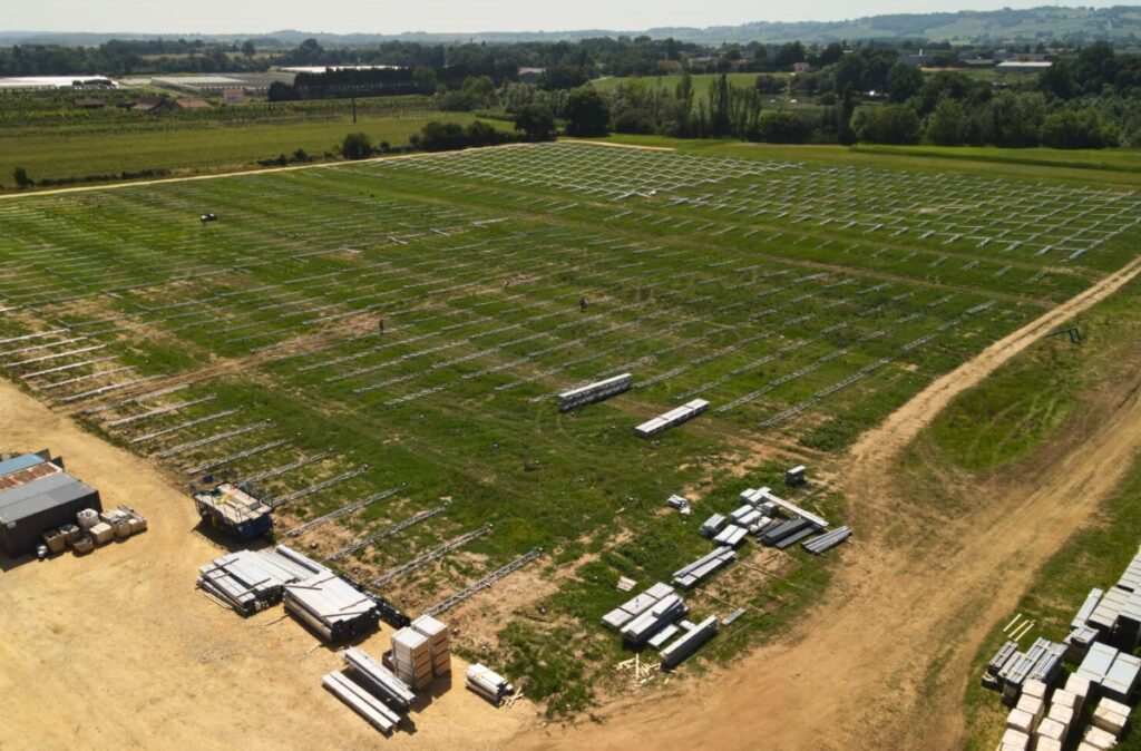 Teren przygotowany pod budowę szklarni, z rozłożonymi elementami konstrukcyjnymi i wyznaczonymi liniami fundamentów.