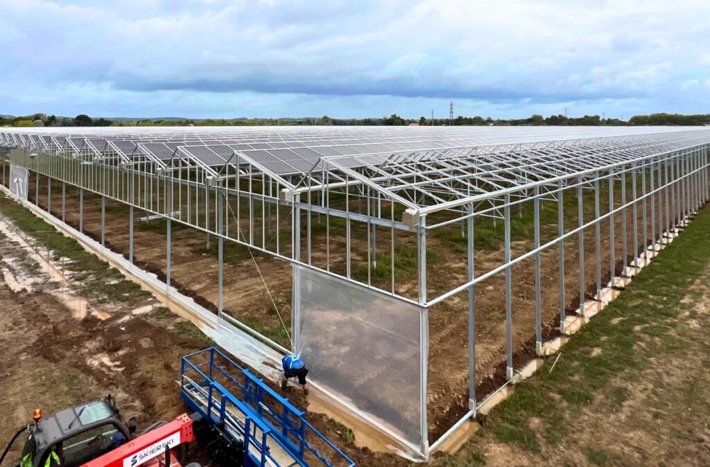 Montaż konstrukcji bocznej szklarni, z widocznymi oszklonymi sekcjami ścian i przygotowaniem pod dalsze szklenie.