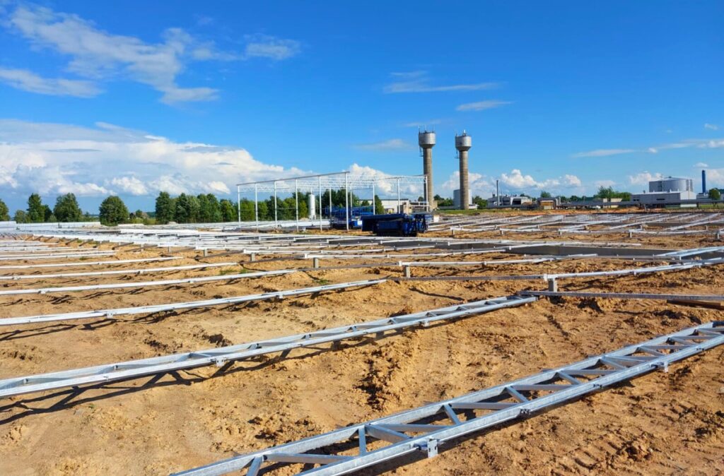 Wczesny etap montażu szklarni z rozłożonymi elementami konstrukcyjnymi na przygotowanym podłożu.