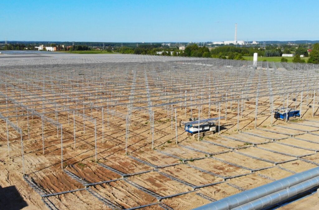 Montaż stalowej konstrukcji szklarni na dużej powierzchni, z widocznymi rzędami słupów.