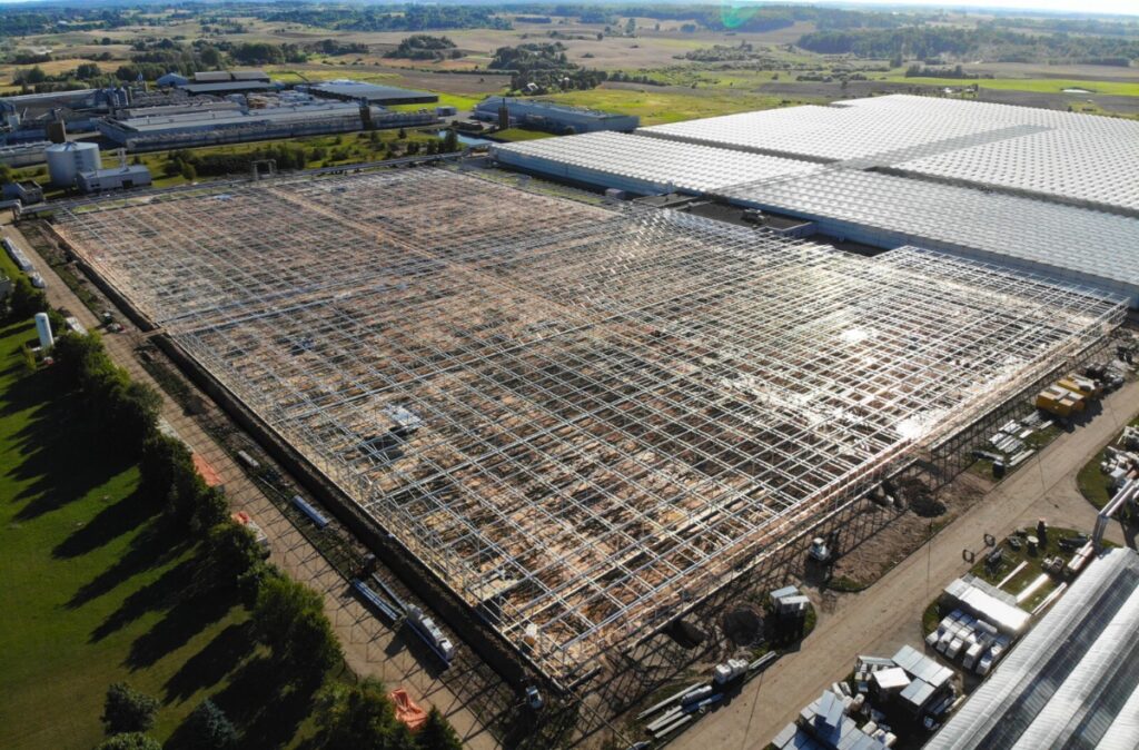 Widok z lotu ptaka na szklarnię w trakcie montażu, z rozbudowaną konstrukcją stalową i częściowo oszklonym dachem.