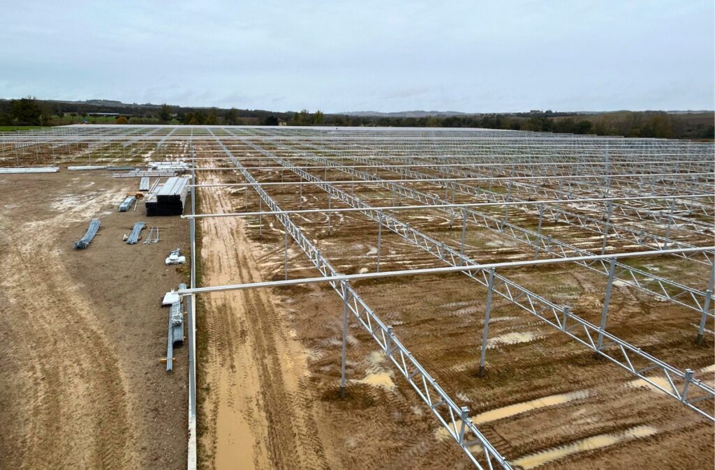 Rozległy plac budowy z montowanymi modułami szklarni – widok na układ konstrukcji rozłożony na dużej powierzchni.