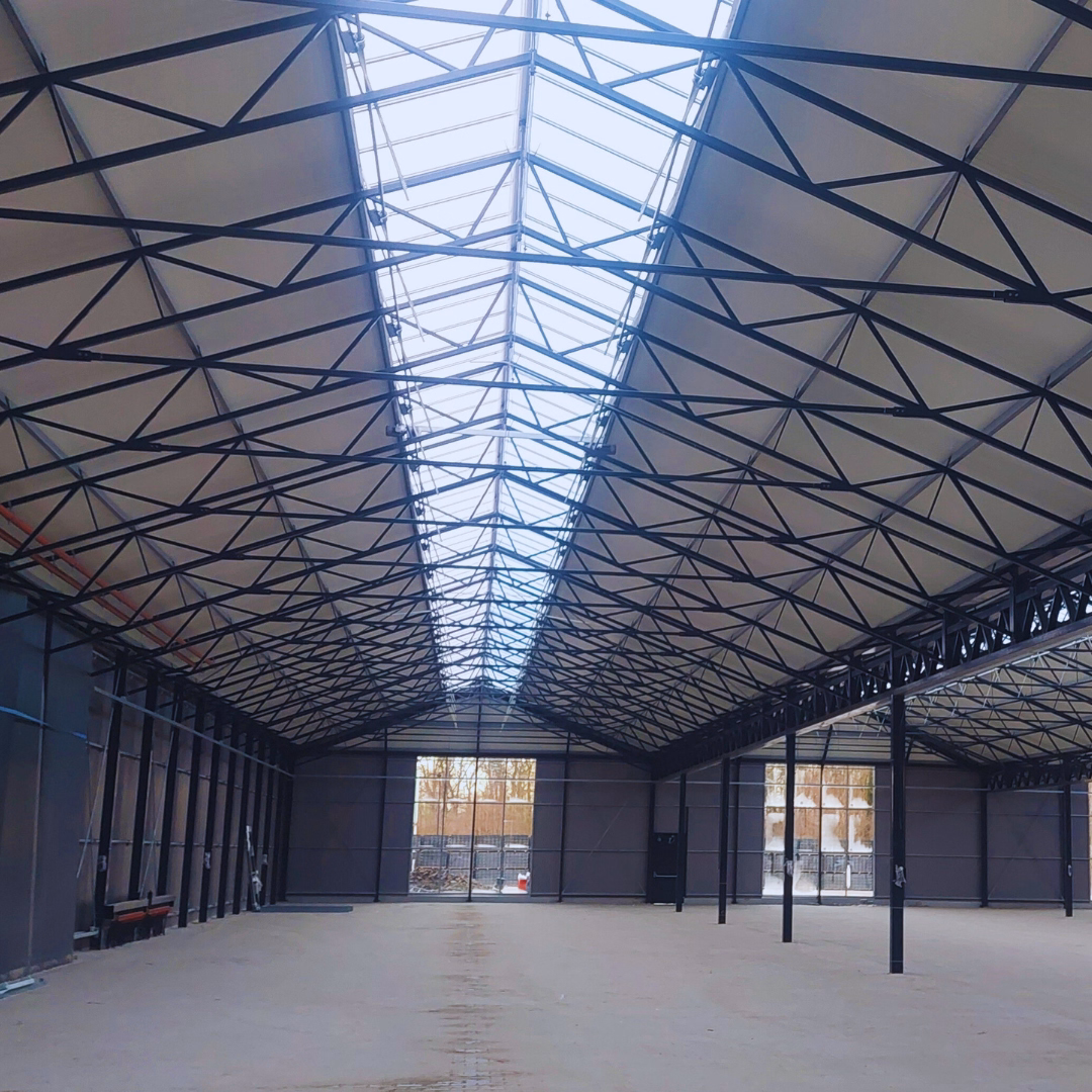 wnętrze hali wielofunkcyjnego centrum ogrodniczego Borghuis: stalowa konstrukcja dachowa, pas świetlików w kalenicy oraz betonowa posadzka