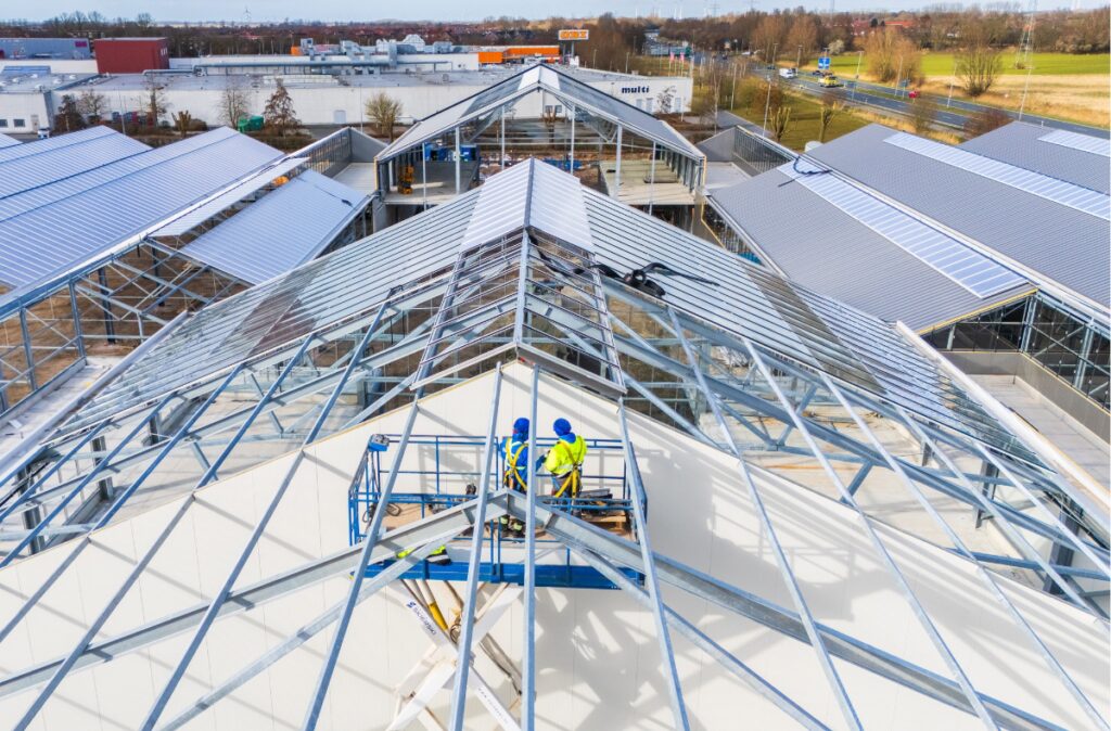 Prace montażowe na dachu centrum ogrodniczego, widoczne instalowanie konstrukcji dachowej przez ekipę pracowników.