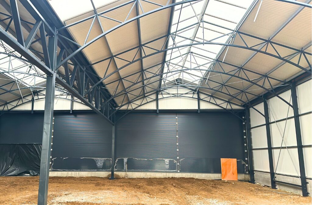 Widok od środka na montaż stalowej konstrukcji dachowej w nowo powstającym dziale ogrodniczym.