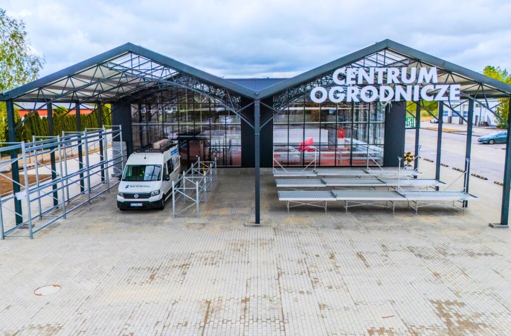 Front nowo wybudowanego działu ogrodniczego PSB Mrówka w konstrukcji szklarniowej, z dużymi przeszkleniami i zadaszoną strefą wejściową.