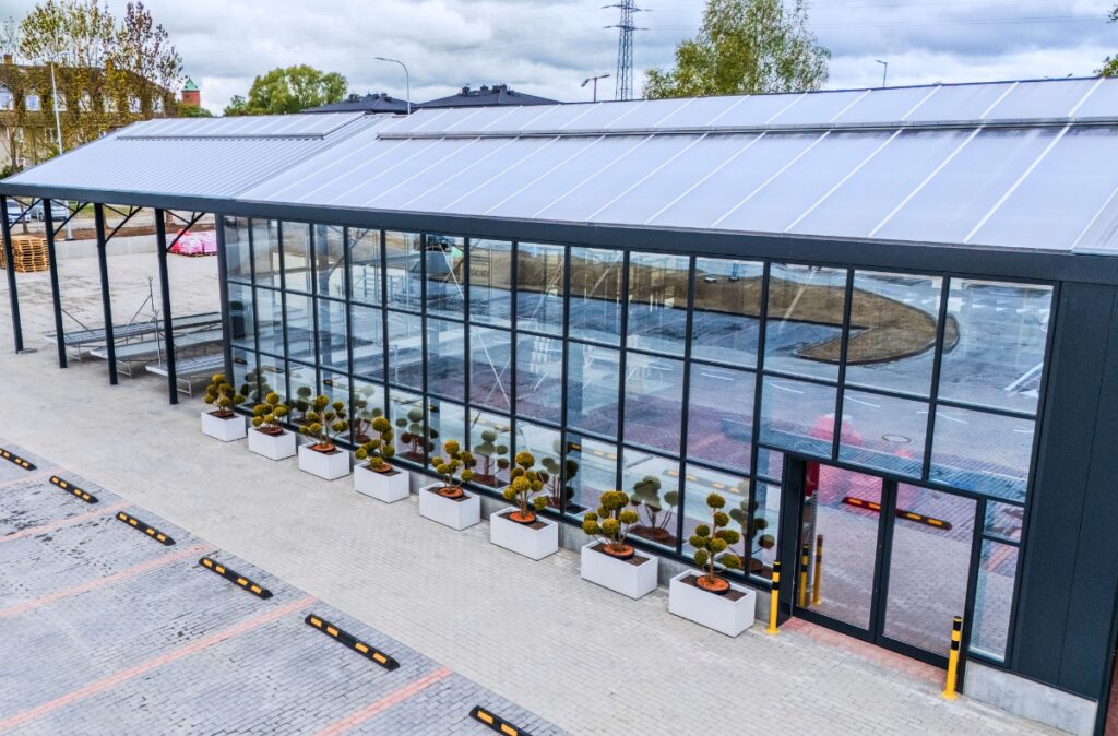 Wykończona boczna elewacja działu ogrodniczego PSB Mrówka w konstrukcji szklarniowej, z dużymi przeszkleniami i gotową aranżacją wejścia.