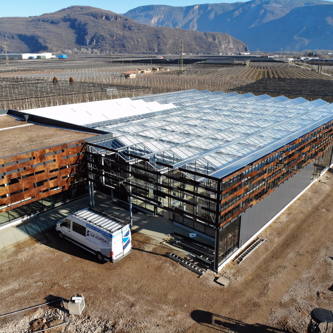 Widok z góry na wolnostojące centrum ogrodnicze w trakcie realizacji, z konstrukcją na bazie szklarni.