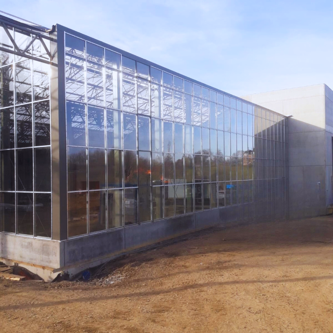 Przeszklona elewacja centrum ogrodniczego Theux – połączenie szklarni z istniejącą halą handlową