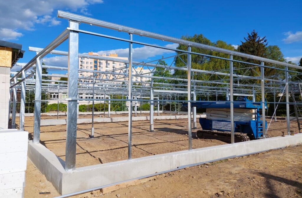 Montaż stalowej konstrukcji szklarni na niskiej podmurówce betonowej.