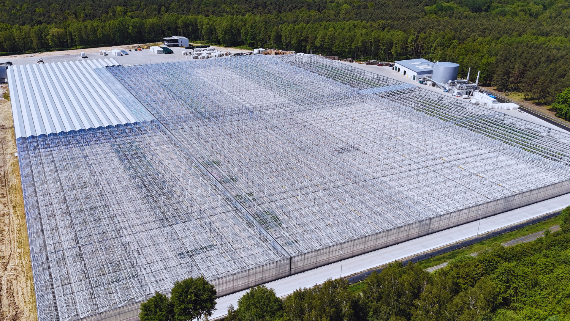 Widok z lotu ptaka na wielkopowierzchniowy kompleks szklarniowy z halą zapleczową i instalacjami technologicznymi.