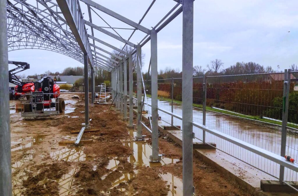Strefa przyścienna szklarni w trakcie budowy, z widoczną konstrukcją stalową i przygotowaniem pod przeszklenia.