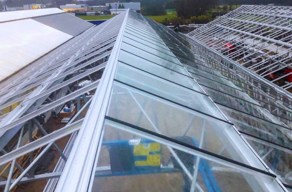 Widok dachu szklarni z przeszkleniami podczas montażu konstrukcji stalowej centrum ogrodniczego w Belgii.