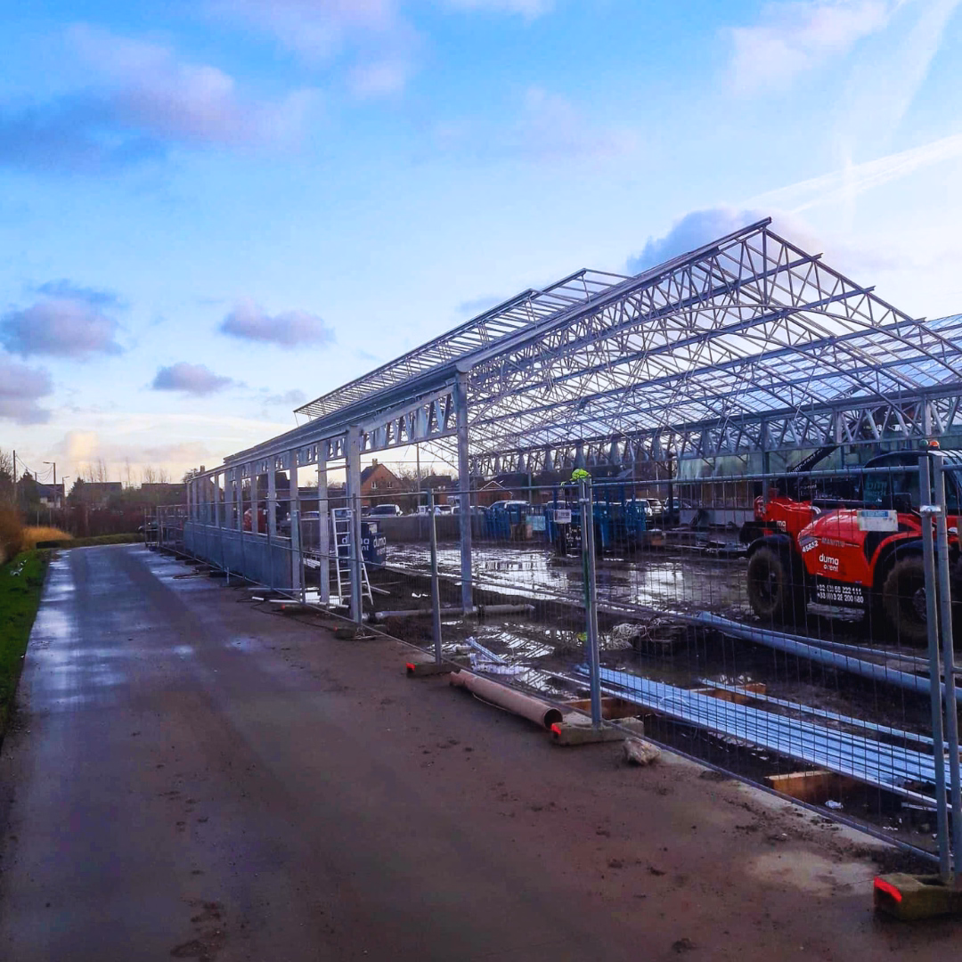 Widok zewnętrzny konstrukcji szklarniowej podczas budowy centrum ogrodniczego Thiels Garden Center w Belgii.
