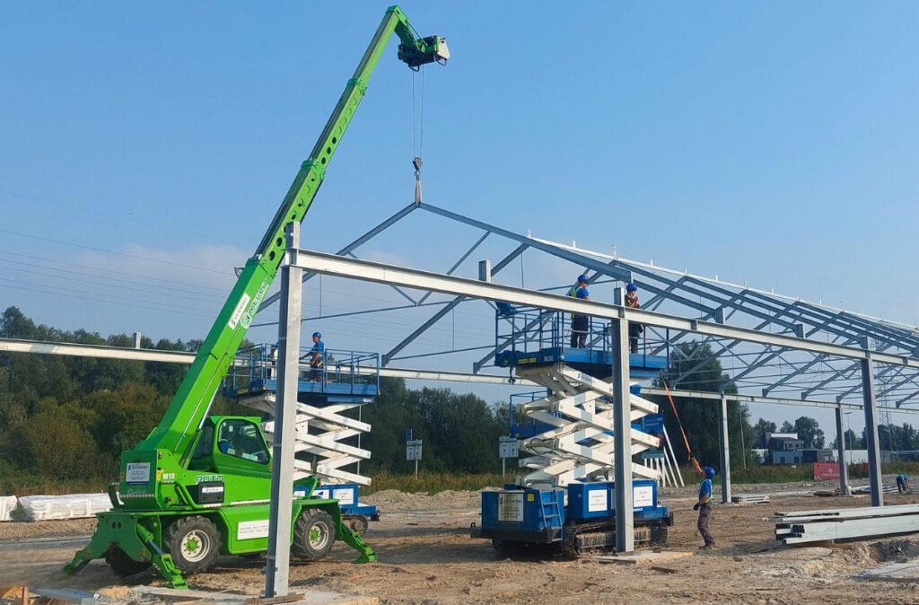 Ładowarka teleskopowa Merlo podczas montażu stalowej konstrukcji centrum ogrodniczego.
