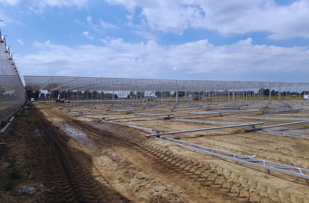 Przygotowanie pod montaż konstrukcji – elementy stalowych kratownic ułożone równolegle na piaskowym podłożu, wyznaczające przyszłe osie obiektu.